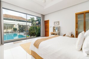 A modern bedroom with a large bed, a desk, and a view of a swimming pool. - Modern 4BR Pool Villa Virginie Naiharn (Rawai)