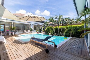 A pool area with lounge chairs, a table, and umbrellas.