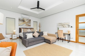 A modern living room with a grey sofa, a coffee table, and a dining area with a wooden table and chair. - Modern 4BR Pool Villa Virginie Naiharn (Rawai)