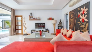 Ein modernes Wohnzimmer mit einem roten Sofa, einem Glastisch, einem Flachbildfernseher und einem großen Gemälde an der Wand.
