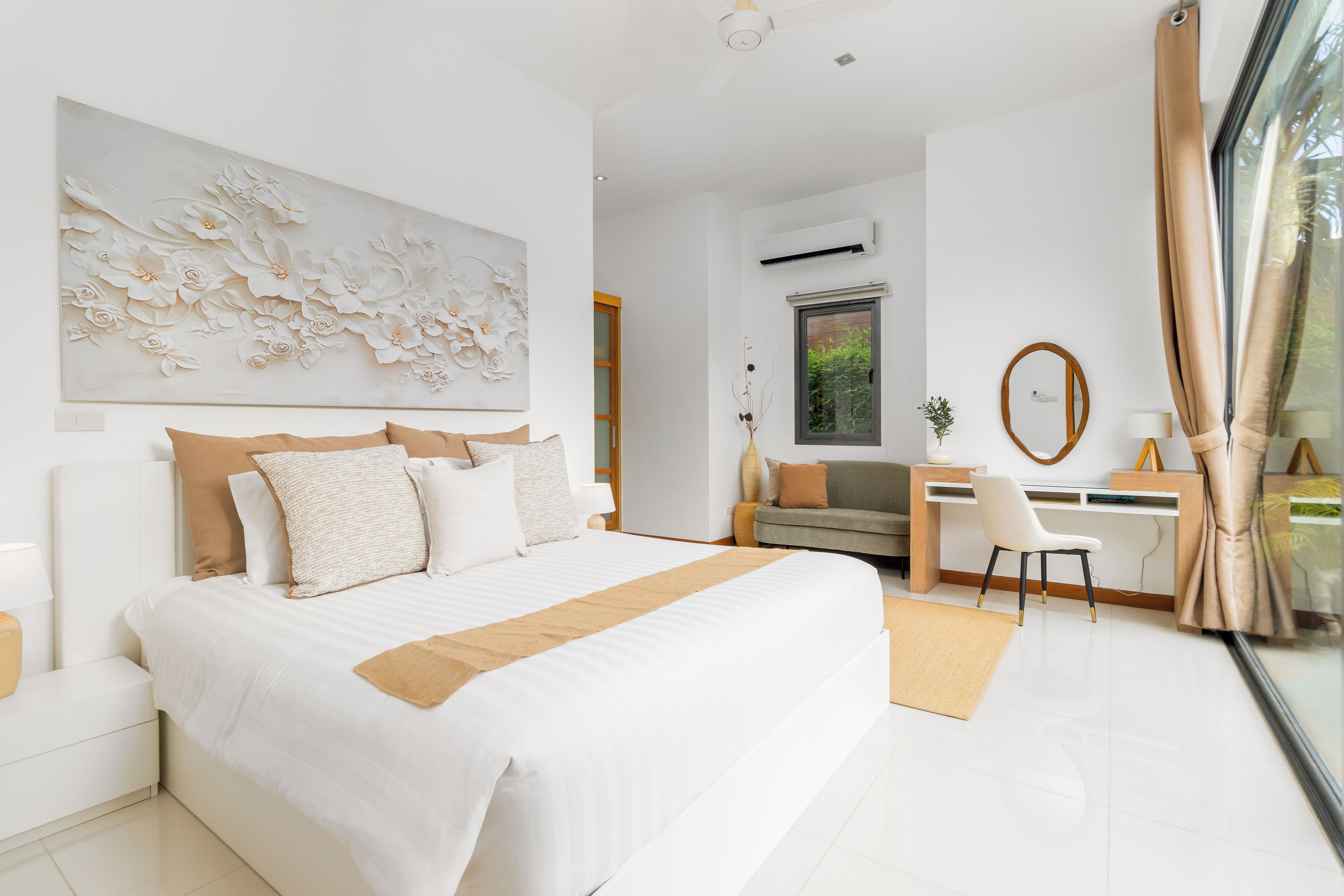 A modern bedroom with a large bed, a desk, and a view of greenery outside.