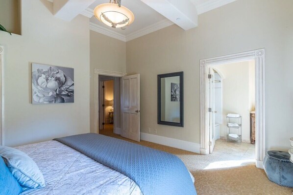 Un dormitorio con una cama grande, una puerta que da a un baño y un pasillo.