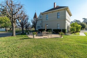 A two-story house with a front yard, a small patio with outdoor furniture, and a tower-like structure on the roof.
