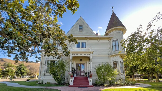 Uma casa grande e histórica com uma torre imponente, varanda frontal e gramado bem cuidado.