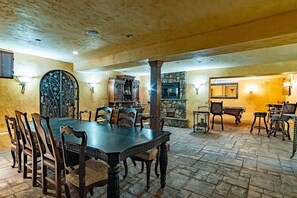 A dining area with a large table and chairs, a stone fireplace, and a stone wall.