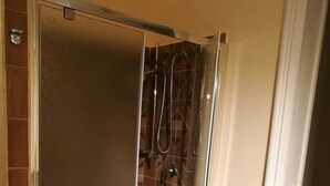 A glass-enclosed shower with a geometric tile pattern on the walls and a green mat on the floor.