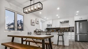 A modern kitchen with a wooden dining table, bar stools, and a stainless steel refrigerator. - Ocean & Bay Views w/ Private Rooftop Hot Tub (San Diego)