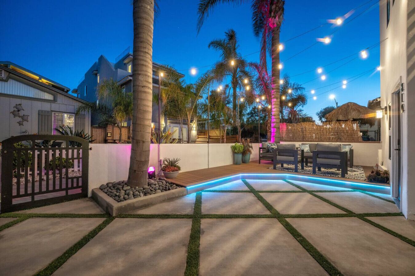 Patio moderno all'aperto con piscina, palme e luci decorative.