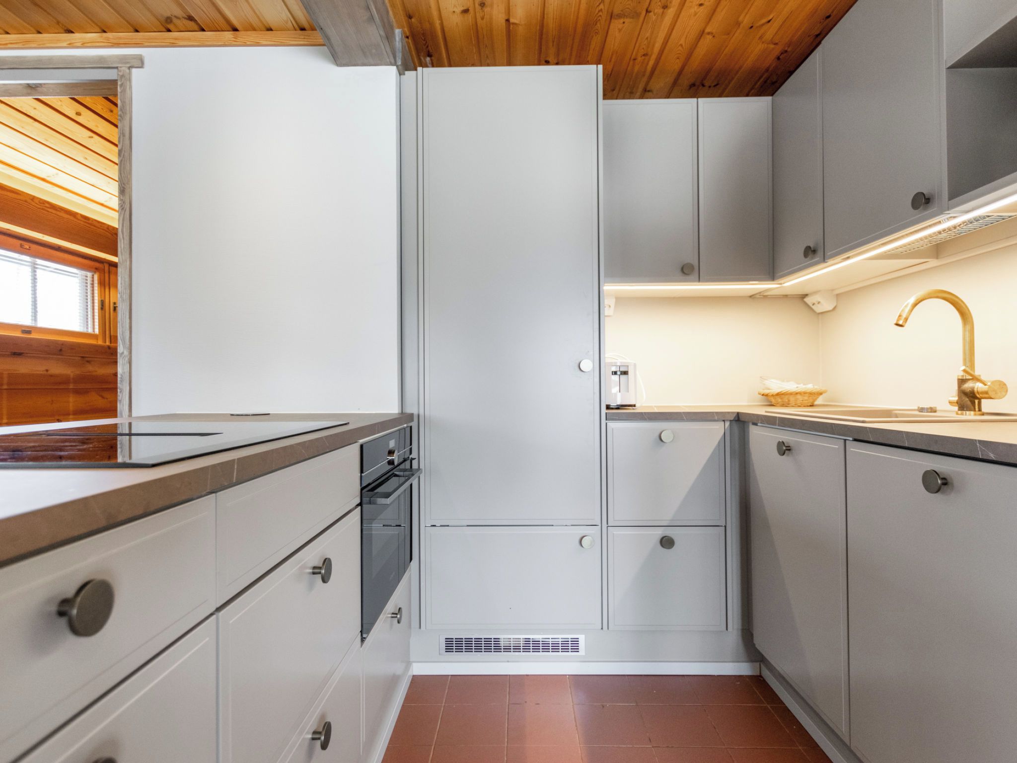Een compacte keuken met inbouwapparatuur, een raam en een houten plafond.