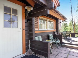 Une cabane en bois avec un porche, une porte dotée d’une fenêtre et des sièges à l’extérieur.