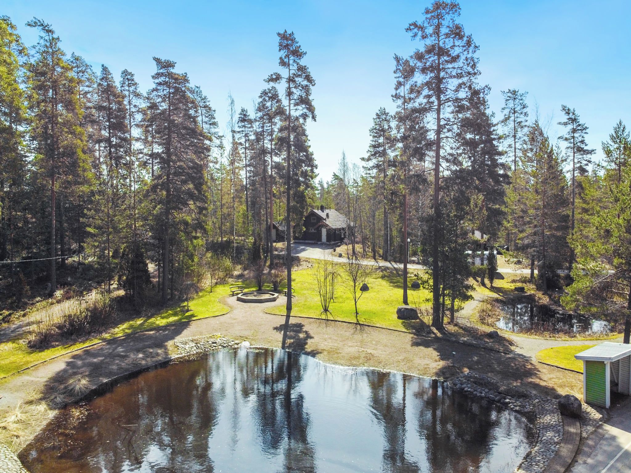 Mökki, jonka ympärillä on metsä ja jonka edessä on lampi.