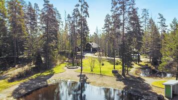 Mökki, jonka ympärillä on metsä ja jonka edessä on lampi.