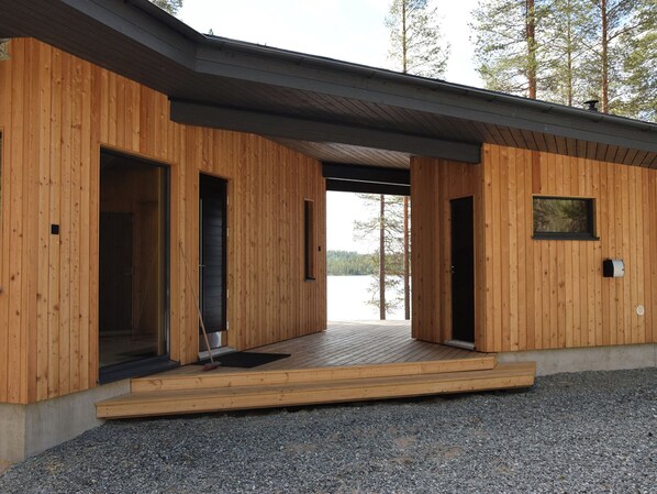 Una cabaña de madera con entrada abierta, un ventanal y vista a un lago.