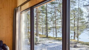 Habitació amb una finestra gran que dona a un paisatge nevàs amb arbres i una massa d'aigua.