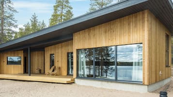A modern wooden cabin with large windows, a deck, and a view of the surrounding forest.