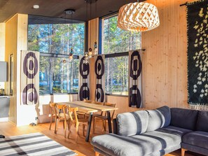 A modern living room with a wooden floor, a dining table with chairs, a sofa, and a large window with curtains.