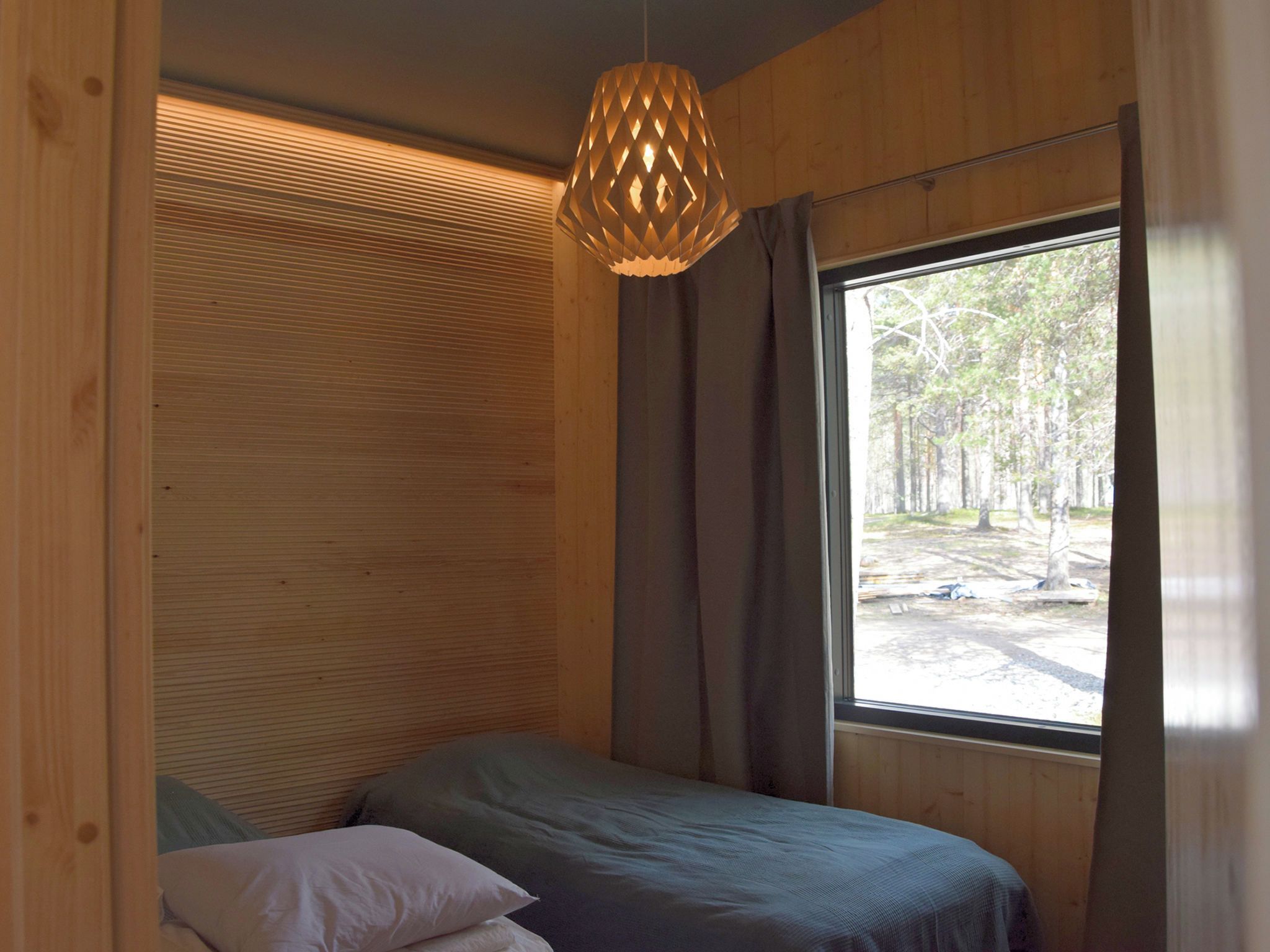 A room with a bed, a hanging light fixture, and a window with a view of trees.