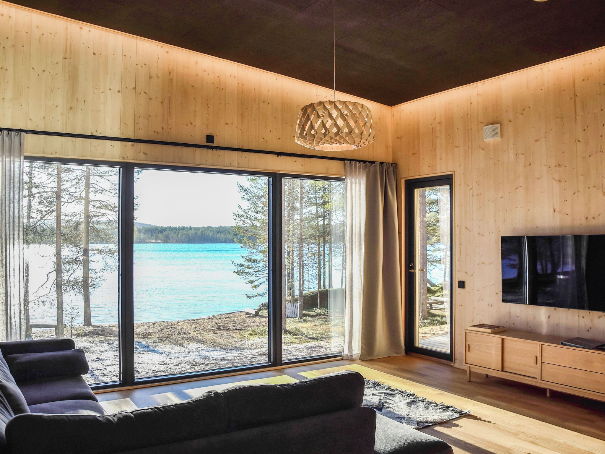 Un moderno salón con ventanas amplias, un sofá, un televisor y un techo de madera.