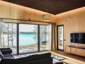 Un moderno salón con ventanas amplias, un sofá, un televisor y un techo de madera.