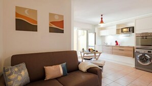 Un salon moderne avec un canapé marron, une petite table sur laquelle est posée une plante, et un coin cuisine équipé d’un lave-linge.