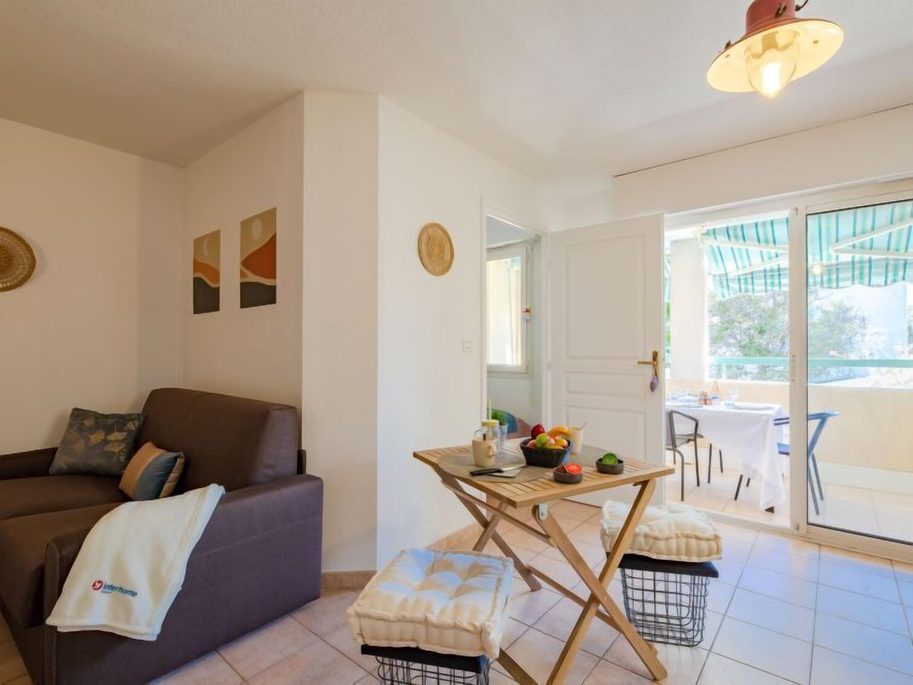 A living room with a sofa, a small table with fruits, and a view of the outside.