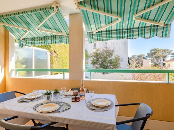 A dining area with a table set for four, a view of the outdoors, and a striped awning above.