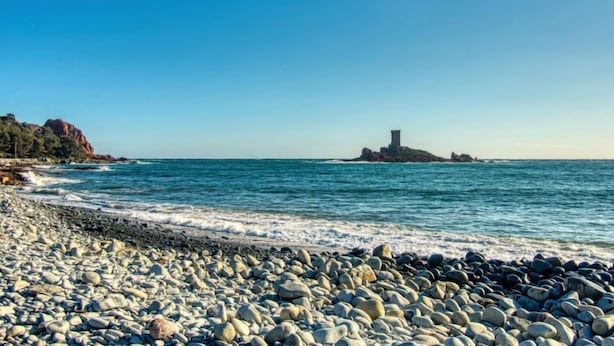 Une plage rocheuse où les vagues se brisent sur le rivage, avec un promontoire rocheux visible au loin.