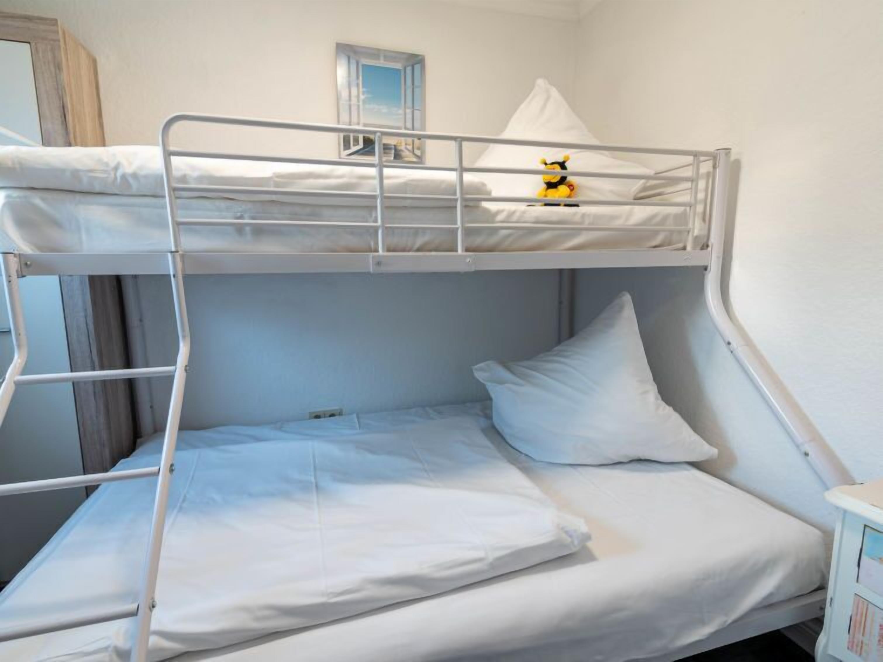 A bunk bed room with white bedding, a small window, and a toy on the top bunk.