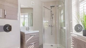 Un baño moderno con cabina de ducha de vidrio, tocador de madera y un espejo grande.
