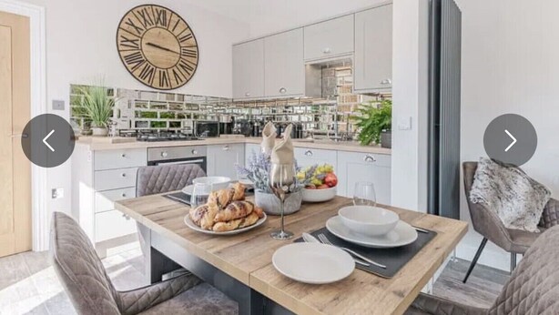 Una cocina moderna con armarios blancos, una mesa de comedor de madera y un reloj de pared grande.