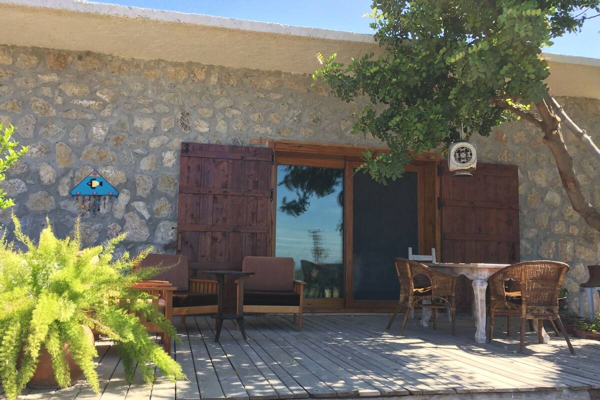 Una terraza de madera con mobiliario exterior, un muro de piedra y una puerta de madera.