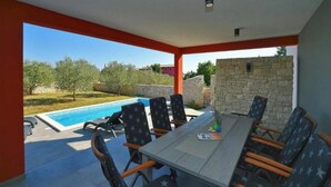 A covered outdoor area with a pool, a dining table with chairs, and a stone wall. - Villa Krnica in Krnica (Marcana)