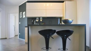 A modern kitchen with two black bar stools, a white countertop, and a bowl of fruit. - Villa Krnica in Krnica (Marcana)