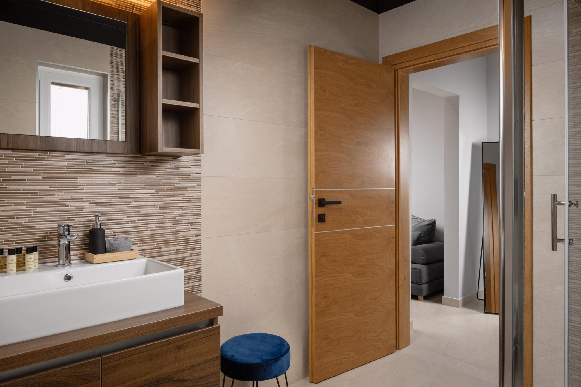 A modern bathroom with a wooden vanity, a large mirror, and a tiled backsplash.