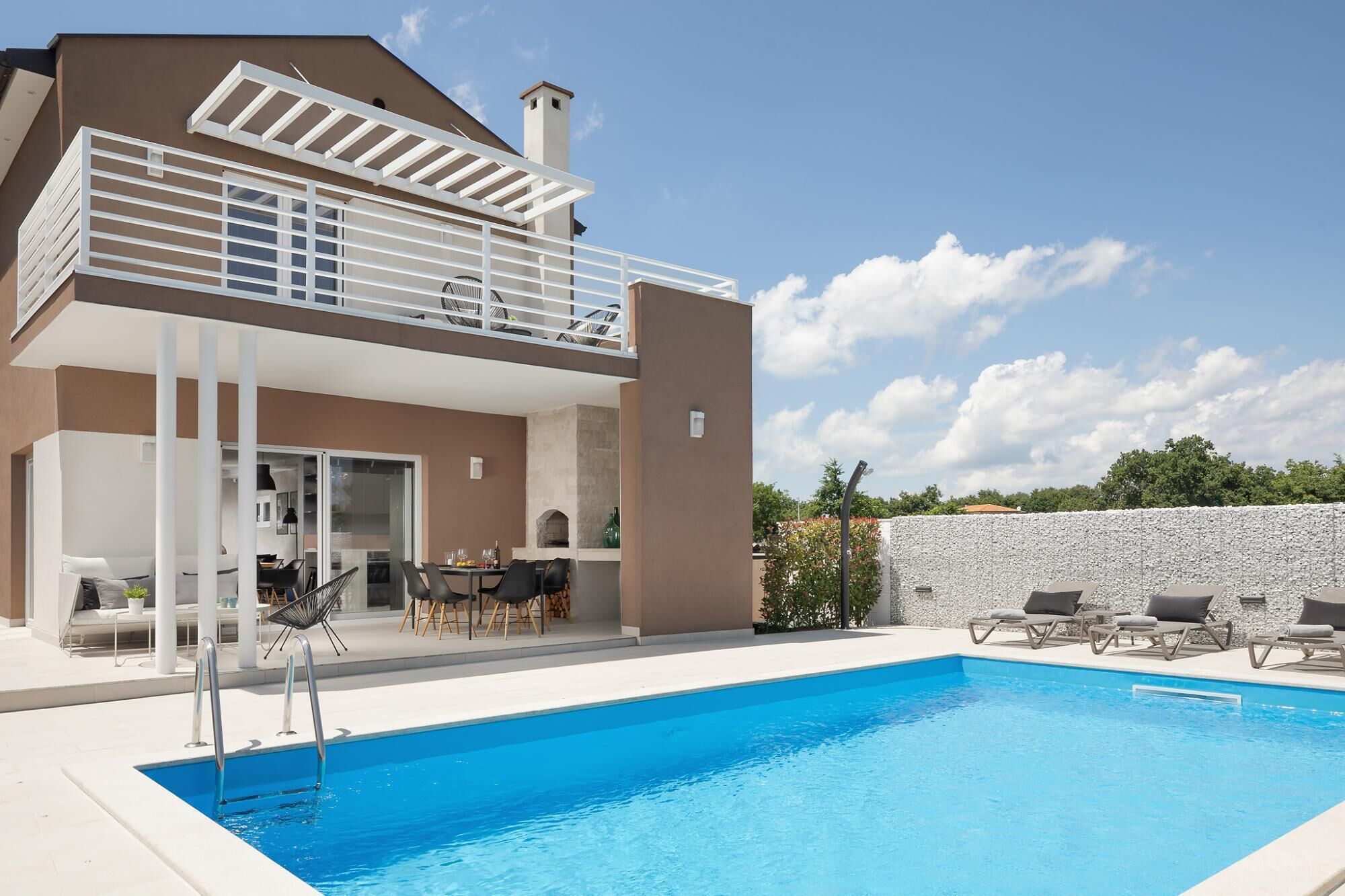 Una casa moderna con piscina, mobiliario exterior y un patio cubierto.
