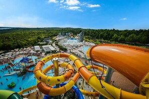 Um parque aquático com várias piscinas e toboáguas, rodeado por vegetação exuberante e um céu limpo.