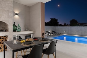 Uma área de refeições ao ar livre com piscina, parede de pedra e espreguiçadeiras.