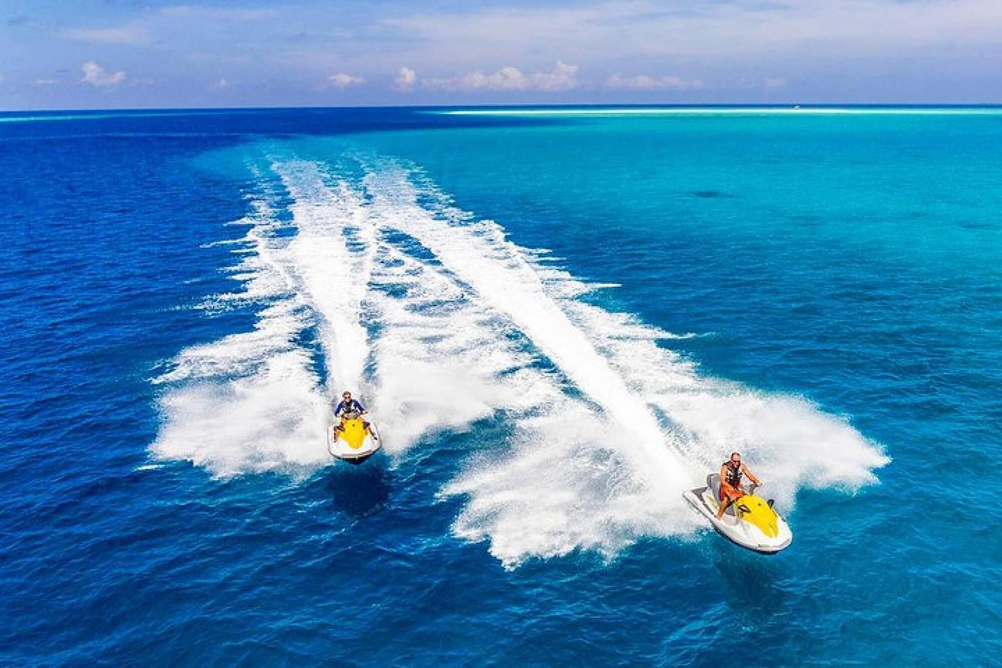 Two jet skis creating white trails in the ocean.