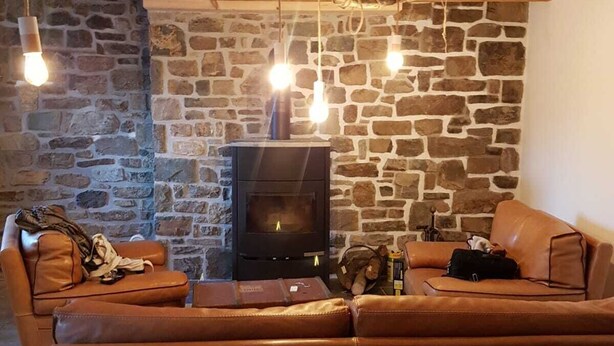 A cozy living room with a stone wall, a fireplace, leather sofas, and hanging light bulbs.