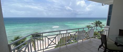 A balcony with a view of the ocean, a table, and chairs.