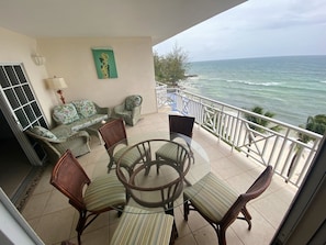 A balcony with wicker furniture, a glass table, and a view of the ocean. - 411 Mistle Cove - Spacious beachfront apartment with large ocean facing balcony (St Lawrence Gap)