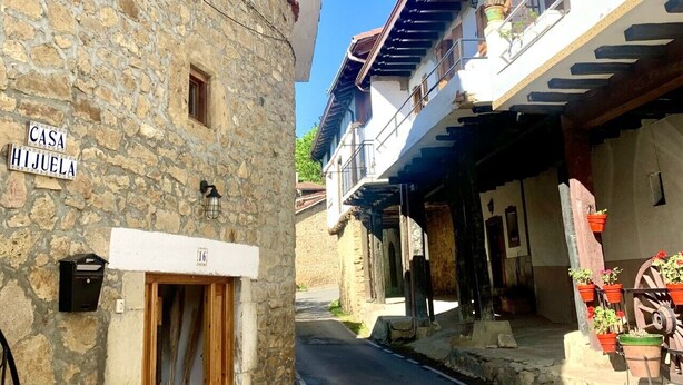 Une rue étroite bordée d’immeubles en pierre, avec une porte en bois et une enseigne indiquant « CASA HIJUELA ».