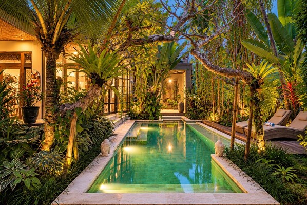 A swimming pool surrounded by lush tropical plants and a building with a glass facade.