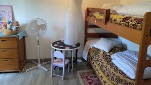 Una camera da letto con letti a castello, una scrivania con sedia, una ventola a piantana e un cesto decorativo con bambole.