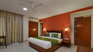 Habitación de hotel con una cama grande, una mesita de noche, un ventilador de techo y un aire acondicionado, además de una puerta.