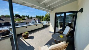 Un balcon avec une table et des chaises, un pot de fleurs et une vue sur les maisons au loin.