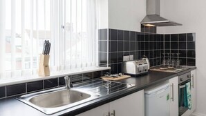 A modern kitchen with black tiles, a stainless steel sink, a toaster, and a window with blinds. - Family Apartment 2nd Floor (Blackpool)