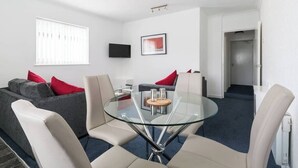 A modern living room with a glass-top coffee table, grey and white sofas, and red cushions. - Family Apartment 2nd Floor (Blackpool)