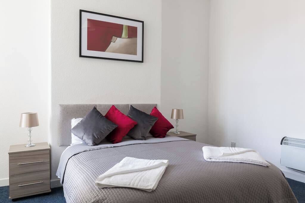 A neatly arranged hotel room with a bed, two bedside tables, a framed picture on the wall, and a radiator.
