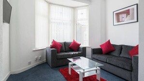 Un salon moderne avec deux canapés gris, des coussins rouges, une table basse en verre et un tapis rouge.